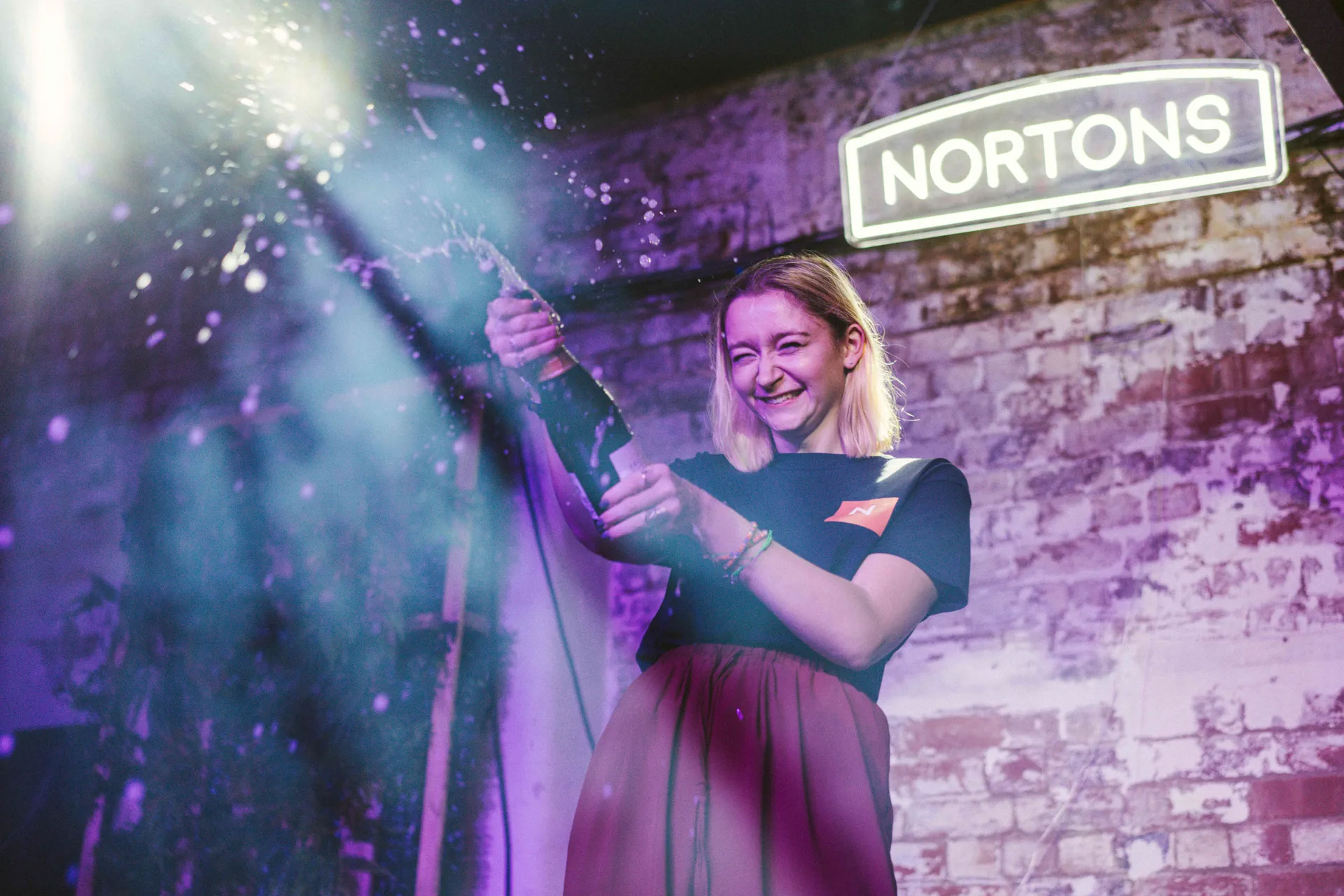 Group celebrating under the glowing Nortons neon sign in Digbeth