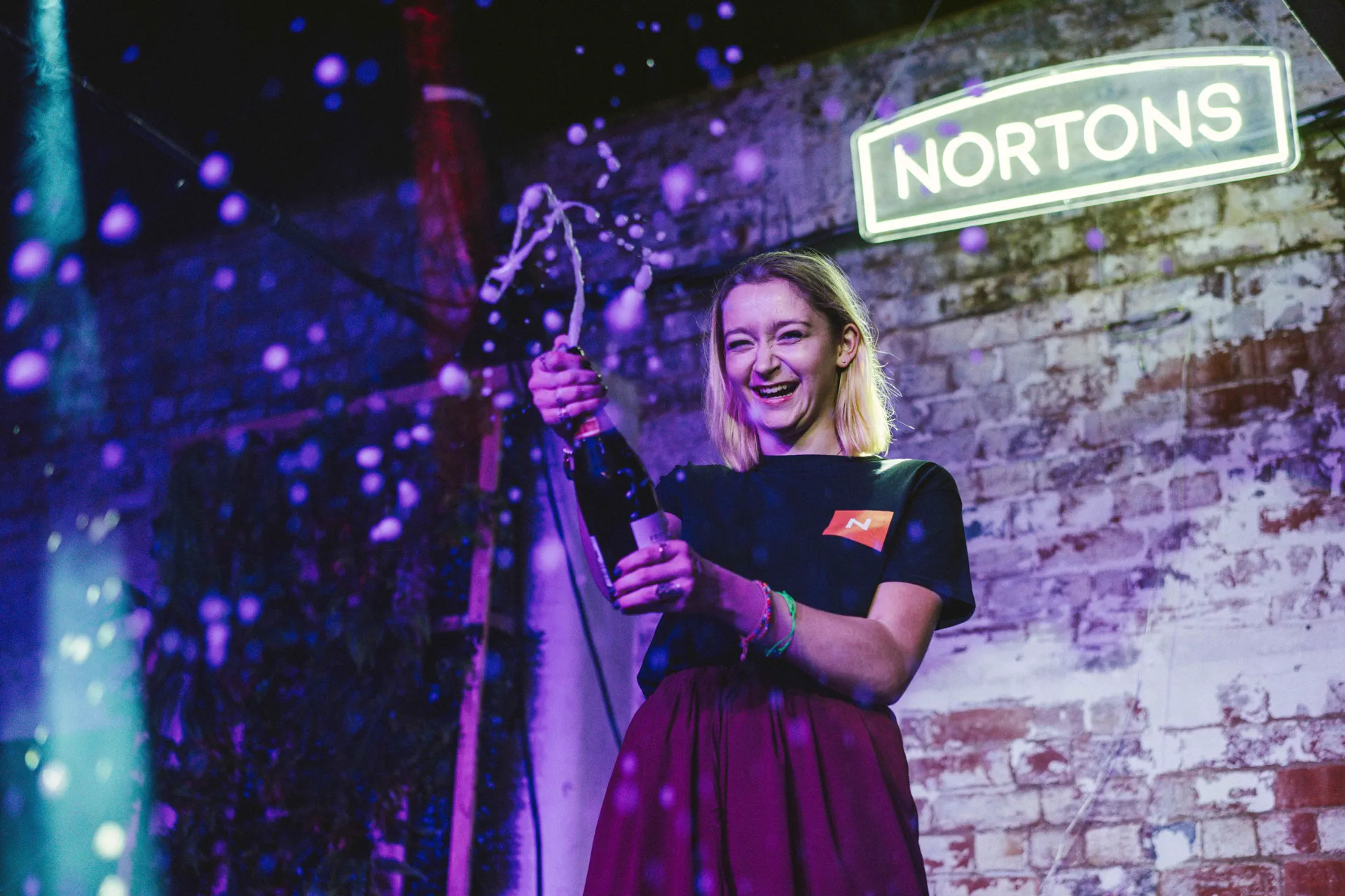 Popping prosecco in front of the glowing Nortons neon sign in Digbeth Birmingham